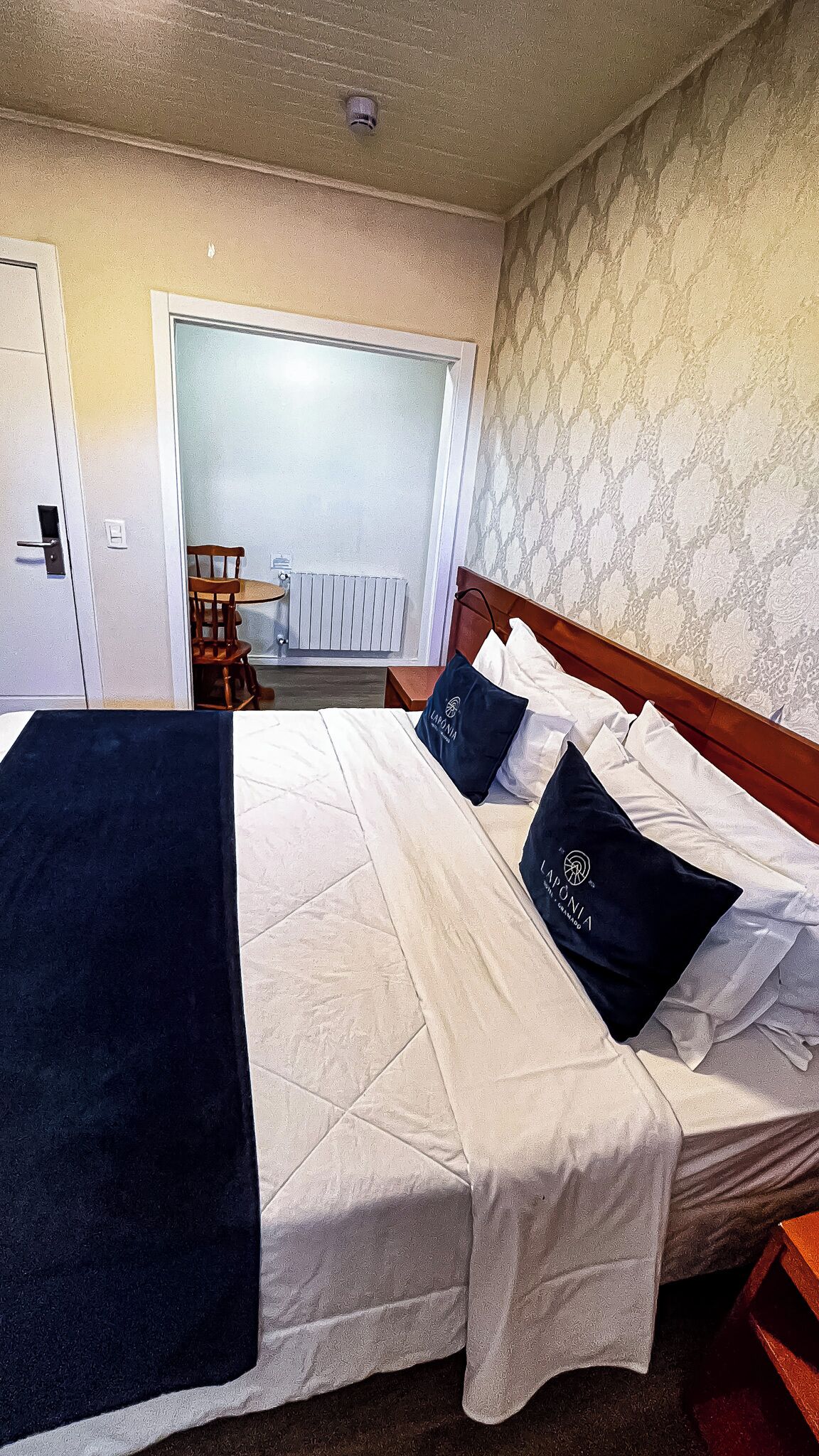 Een hotelkamer met een bed, een stoel, een radiator en een deur.