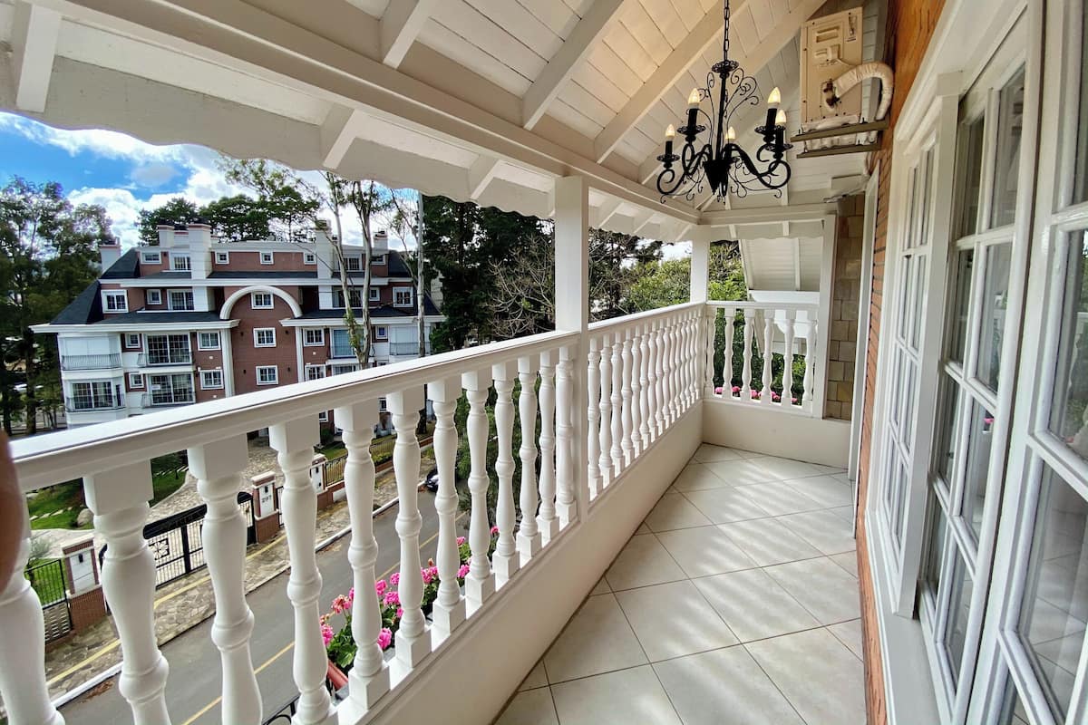 A covered balcony with white balustrades, a chandelier, and a view of a multi-story house.