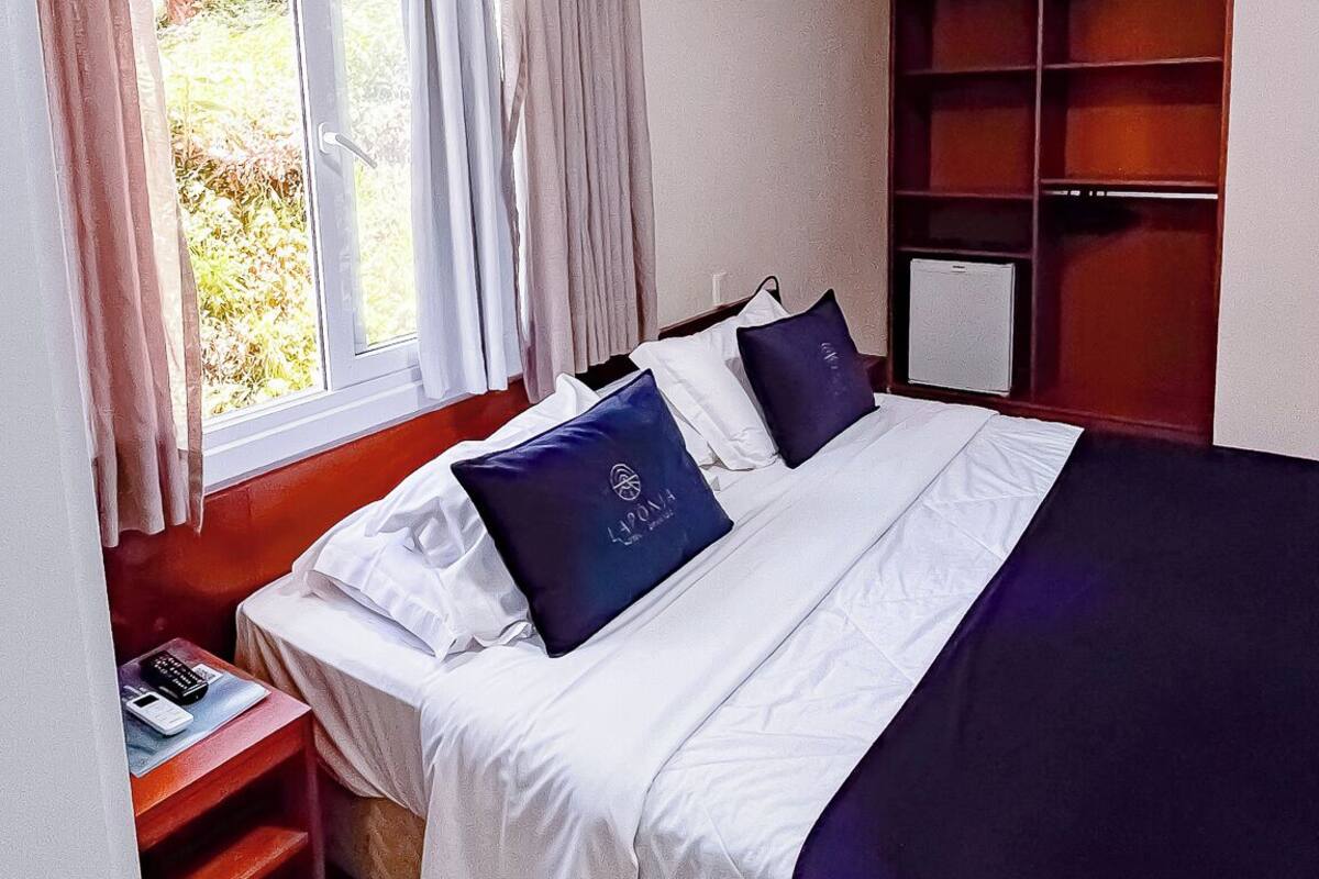 A hotel room with a bed, a window with curtains, a bedside table with a phone, and a built-in wardrobe.
