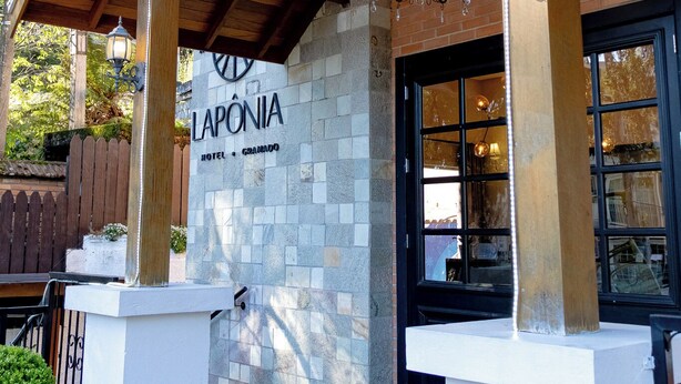 Een hotelentree met een overdekte veranda, een stenen muur en een bord waarop 'LAPONIA HOTEL + GRADINHO' staat.