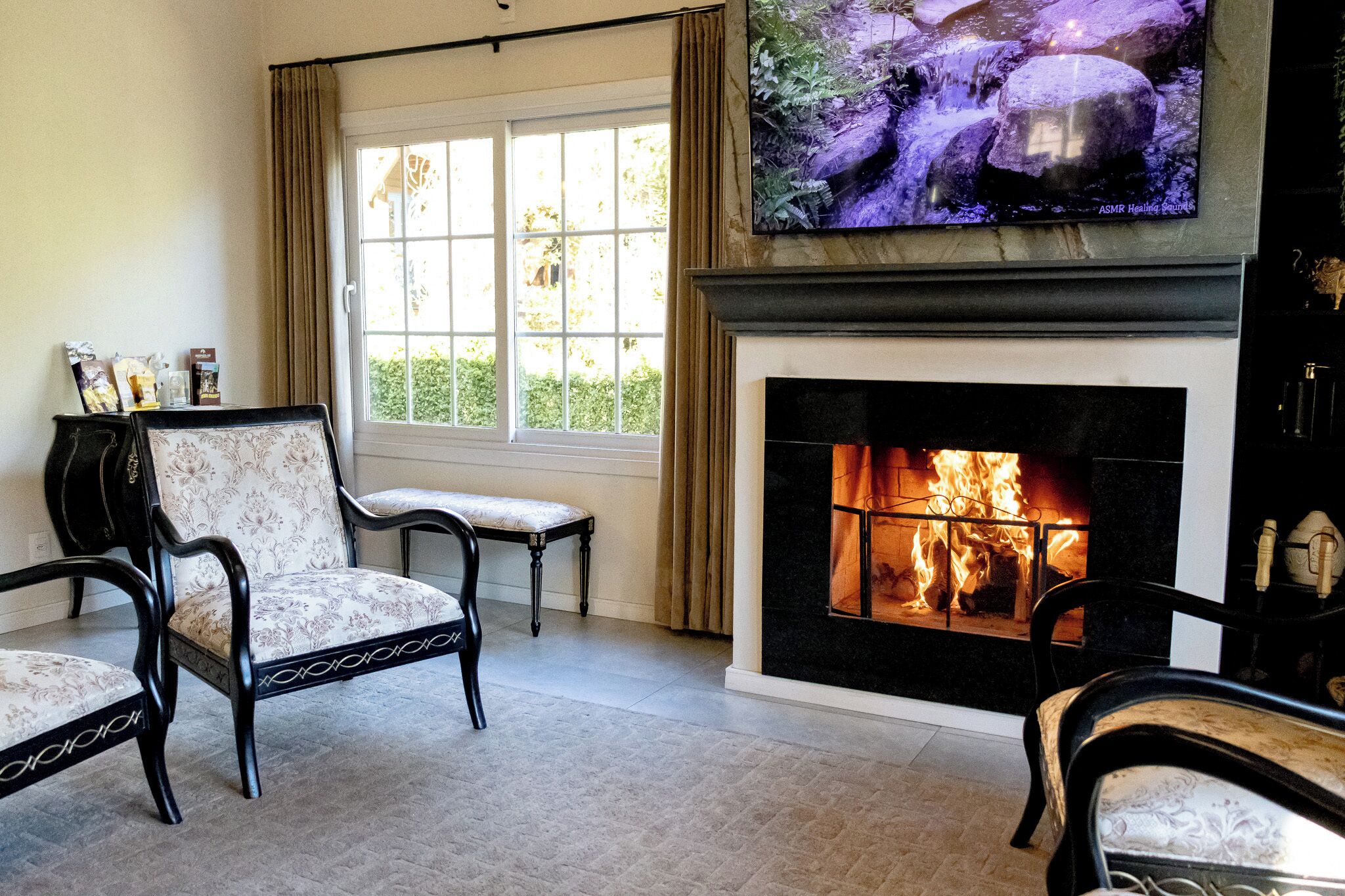 Una sala de estar con chimenea, un televisor montado encima y una ventana con cortinas.