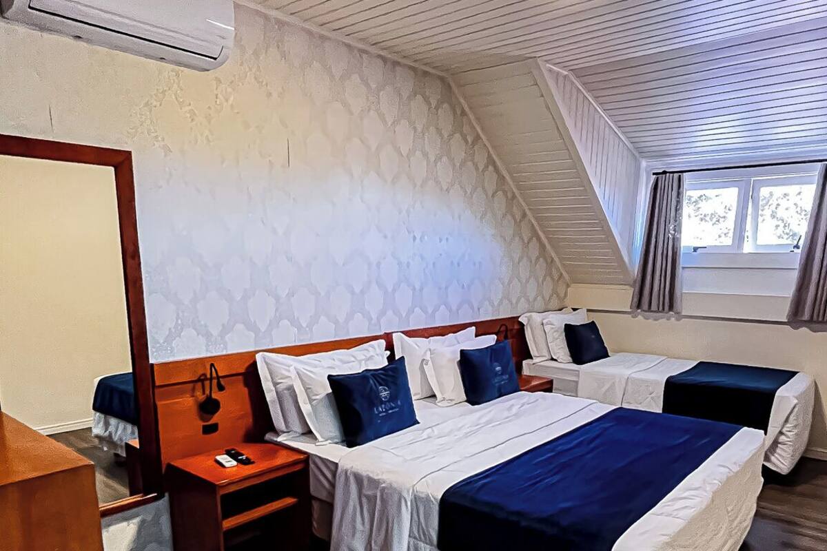 A hotel room with two beds, a wooden desk, a mirror, and an air conditioning unit.