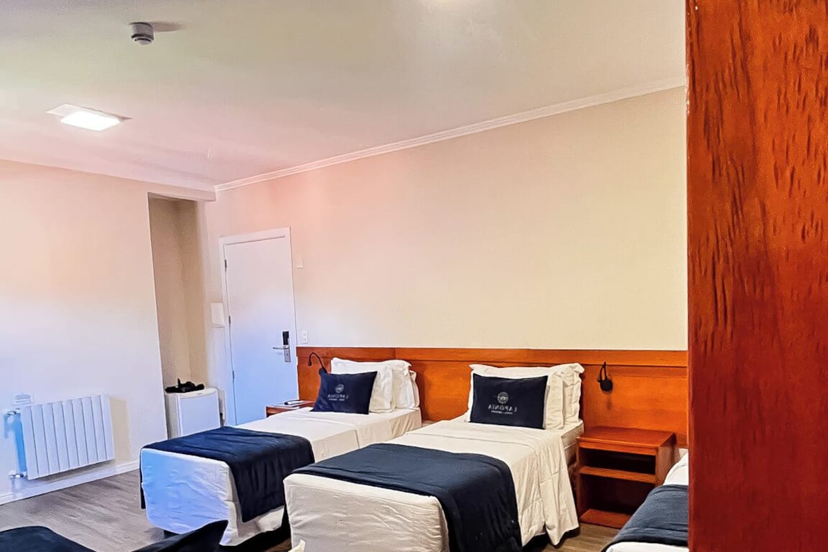 A hotel room with four beds, a wooden headboard, a white radiator, and a door.