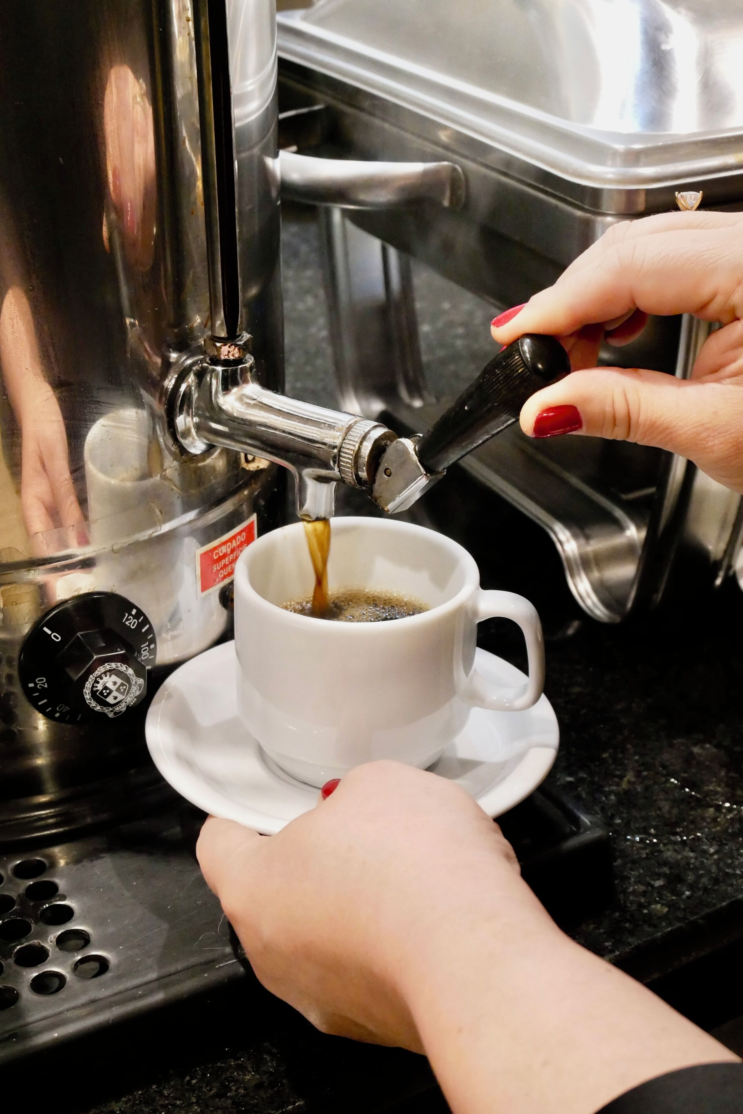 Una persona usando una cafetera, sirviendo café en una taza.