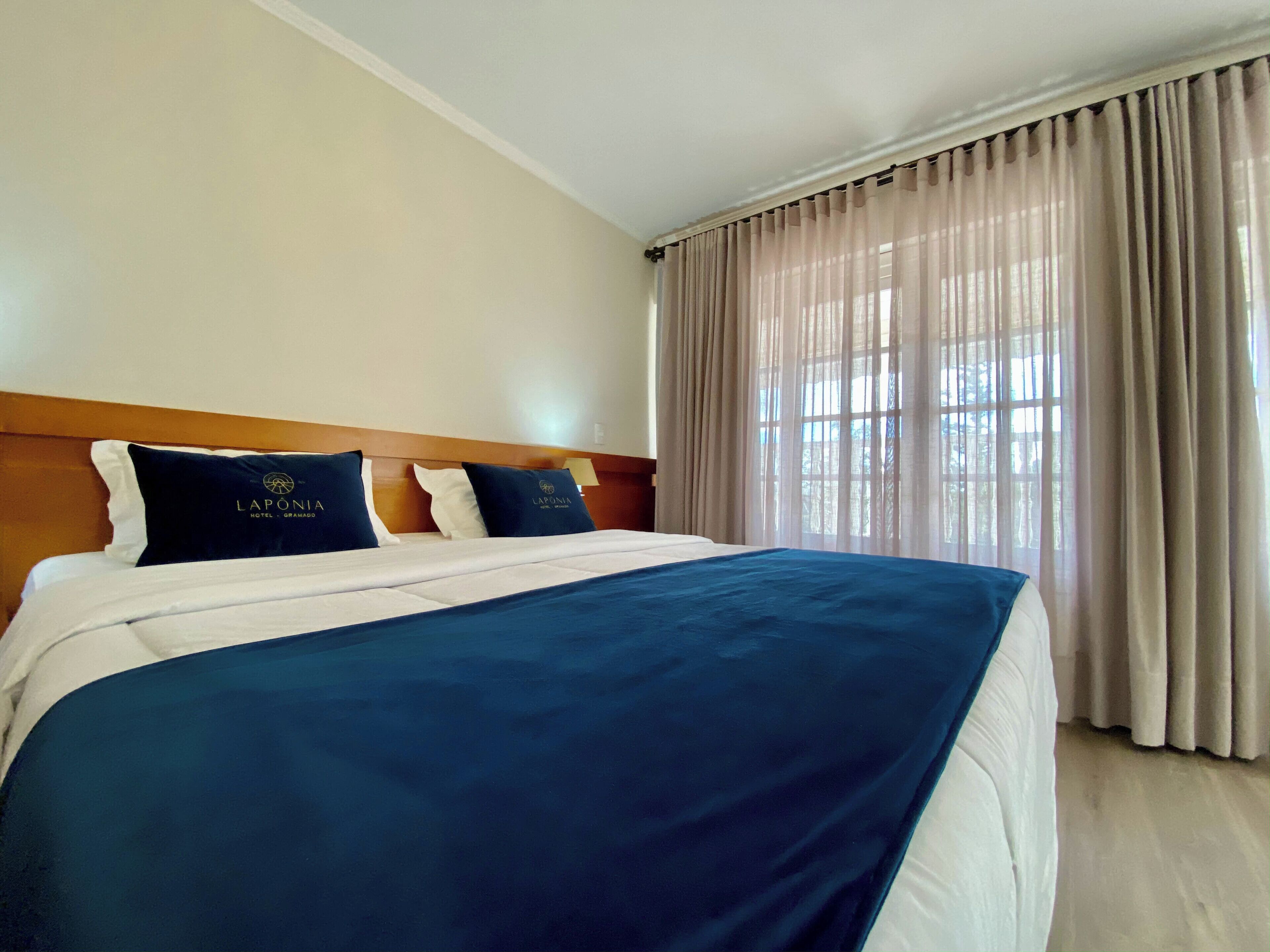 Una habitació d'hotel amb un llit gran, un capçal i una finestra amb cortines.