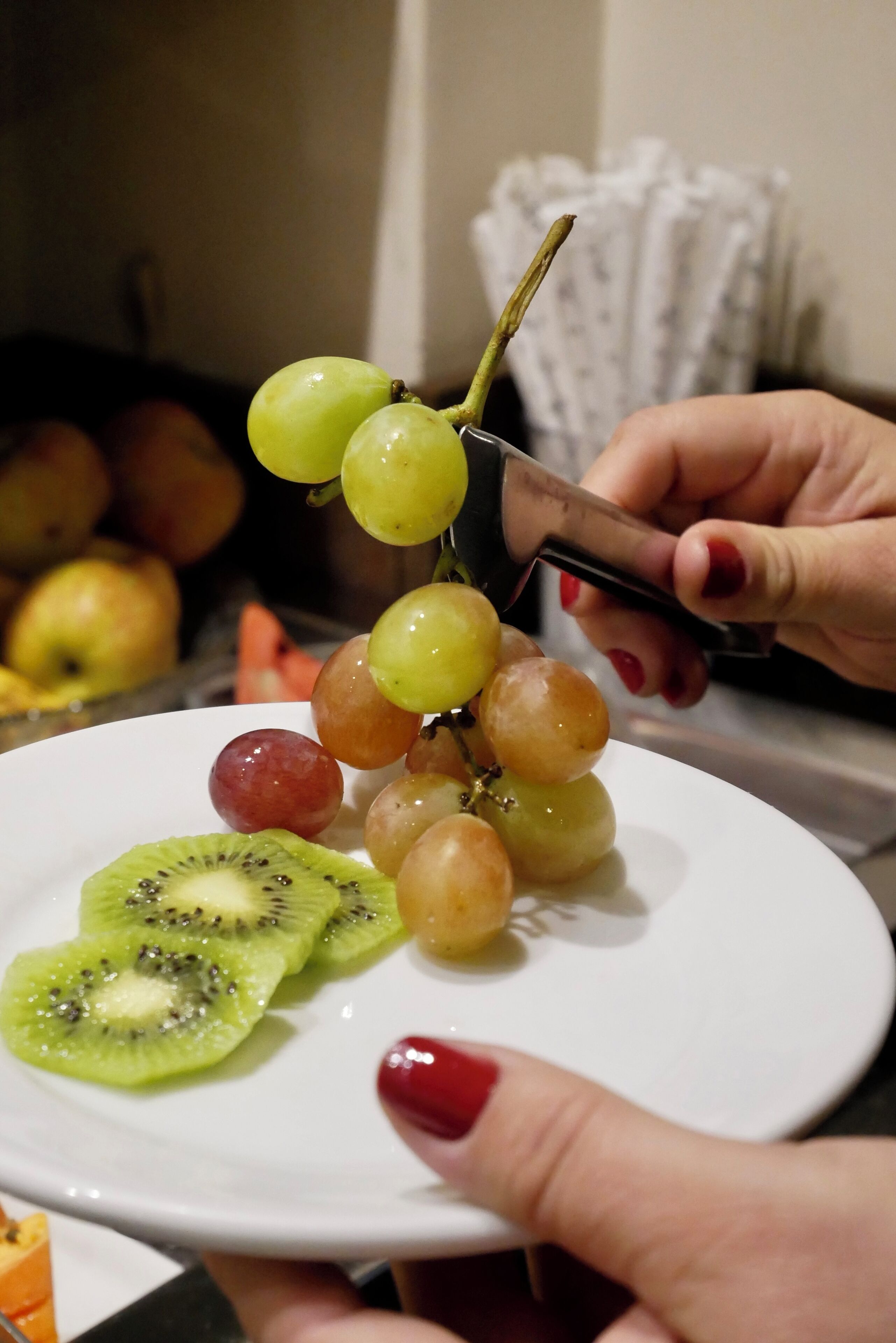 Una mano sosteniendo un cuchillo cortando un racimo de uvas en un plato blanco.
