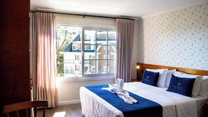 Een hotelkamer met een groot raam, een bed met blauw beddengoed en uitzicht op gebouwen.