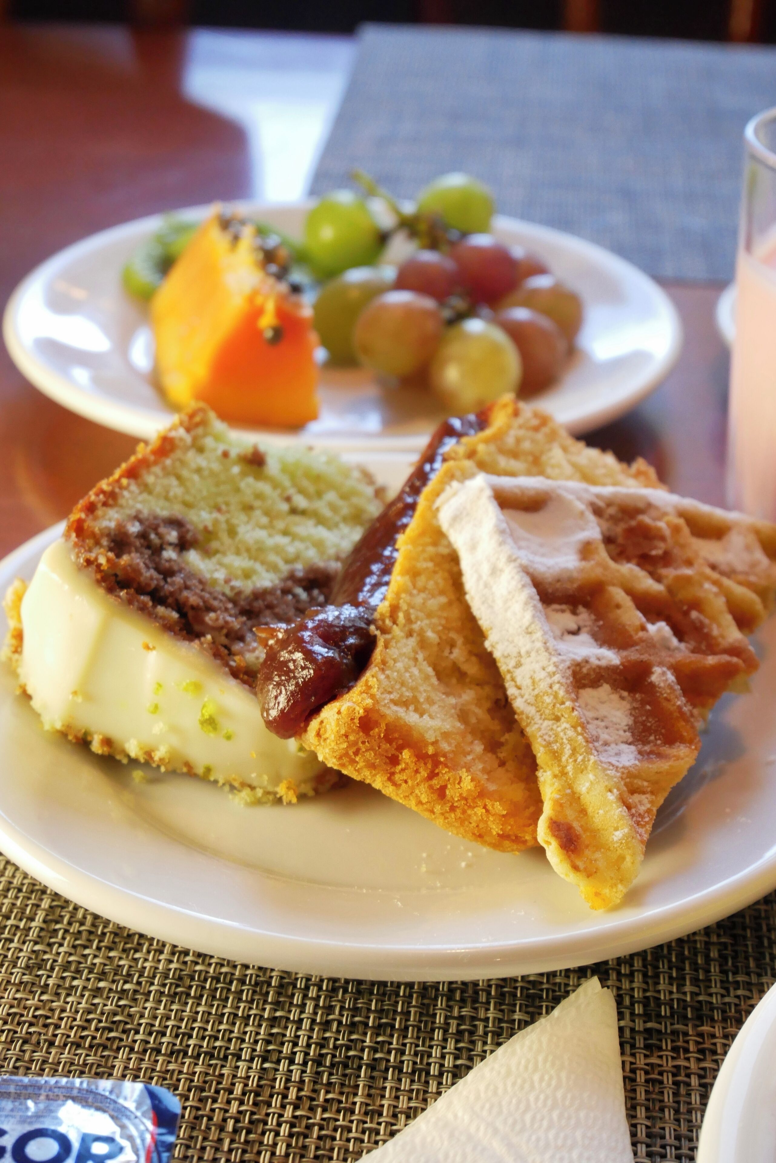A plate with a slice of cake, a piece of bread with jam, and a plate of fruit.