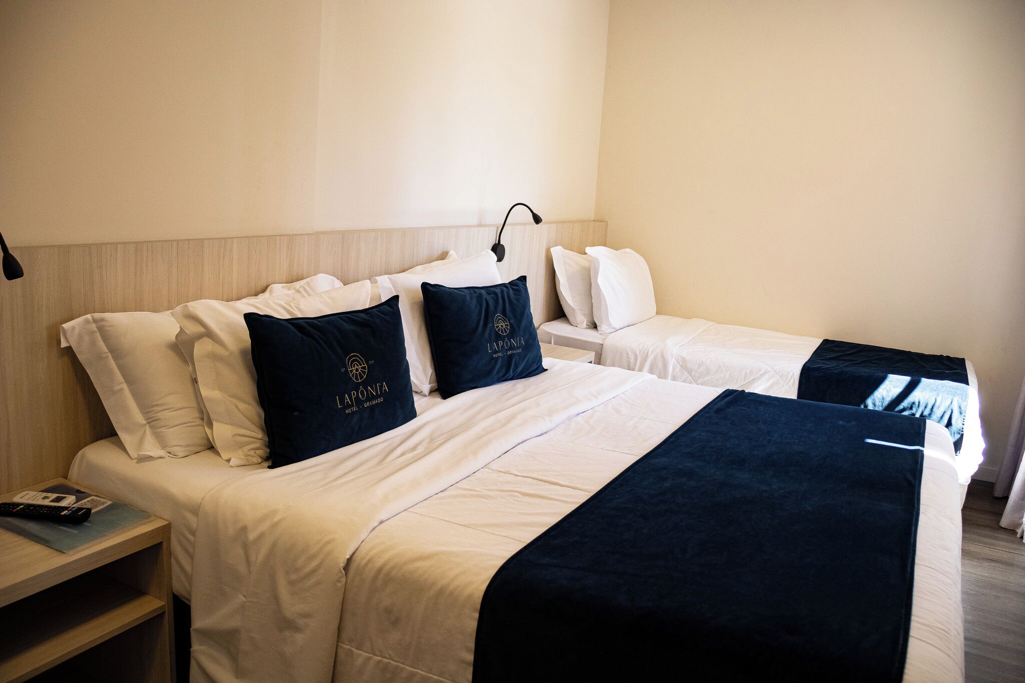 A hotel room with two beds, each with white bedding and navy blue throw pillows.