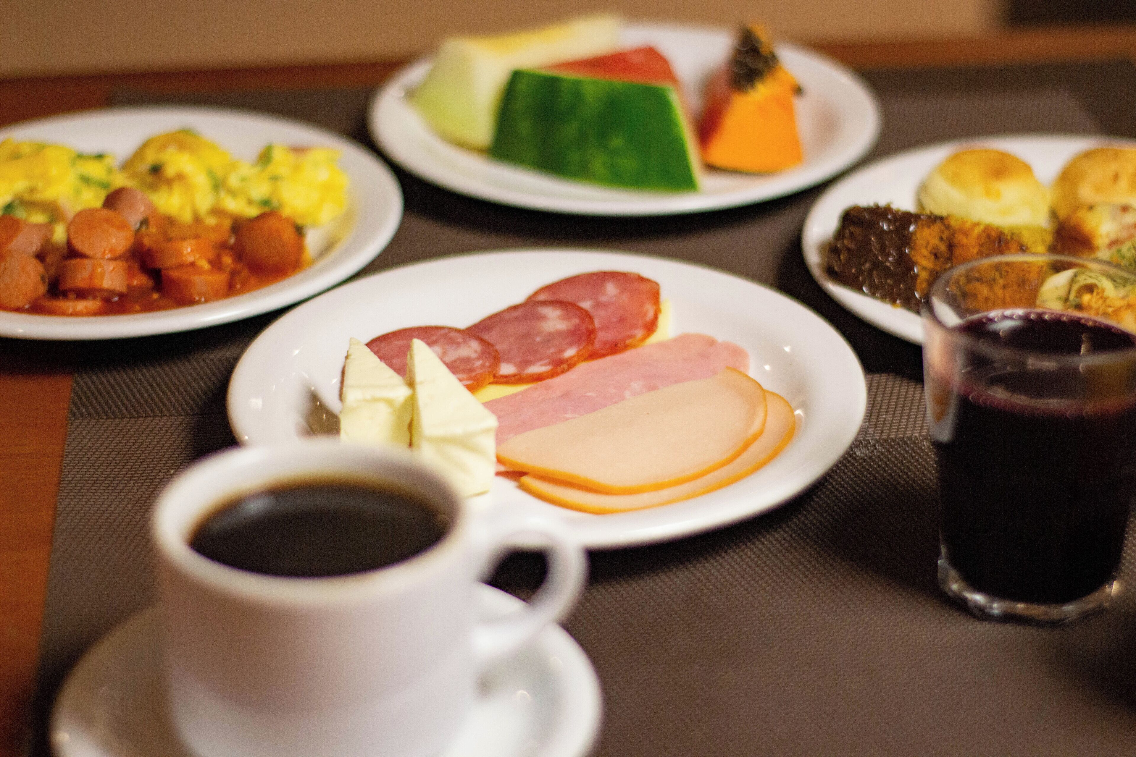 Una mesa con platos de comida, una taza de café y un vaso de bebida oscura.