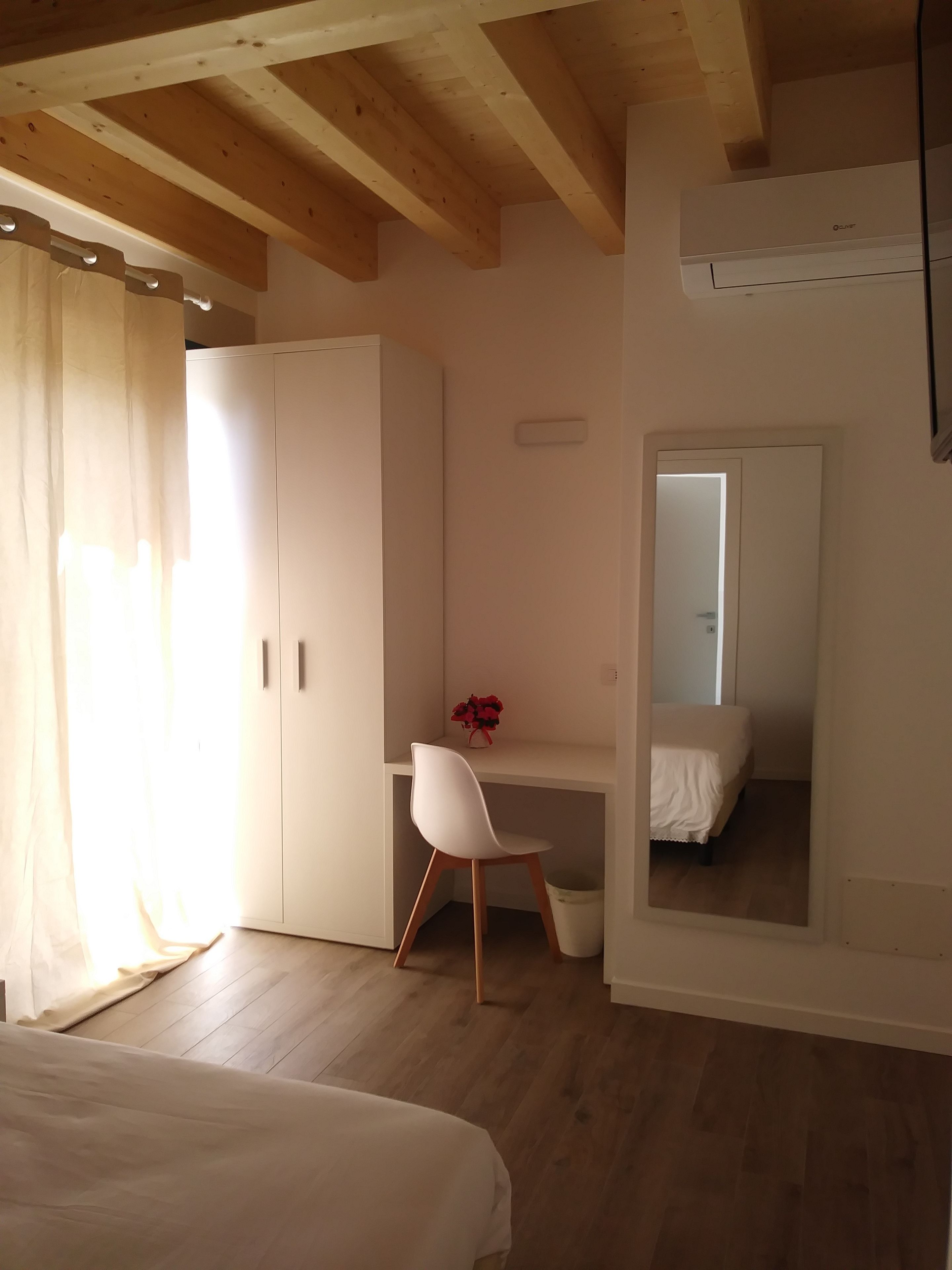 A bedroom with a bed, a desk, a chair, a wardrobe, and a mirror.
