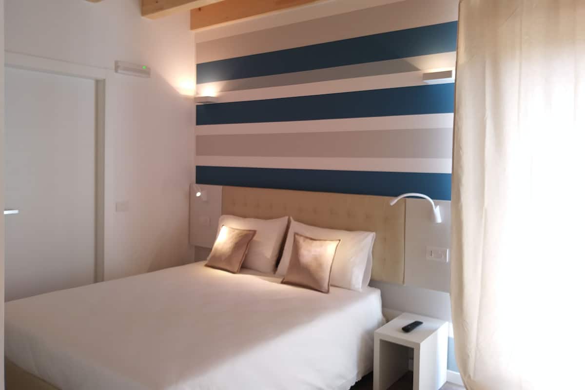 Un dormitorio con cama, mesita de noche y pared con rayas horizontales.