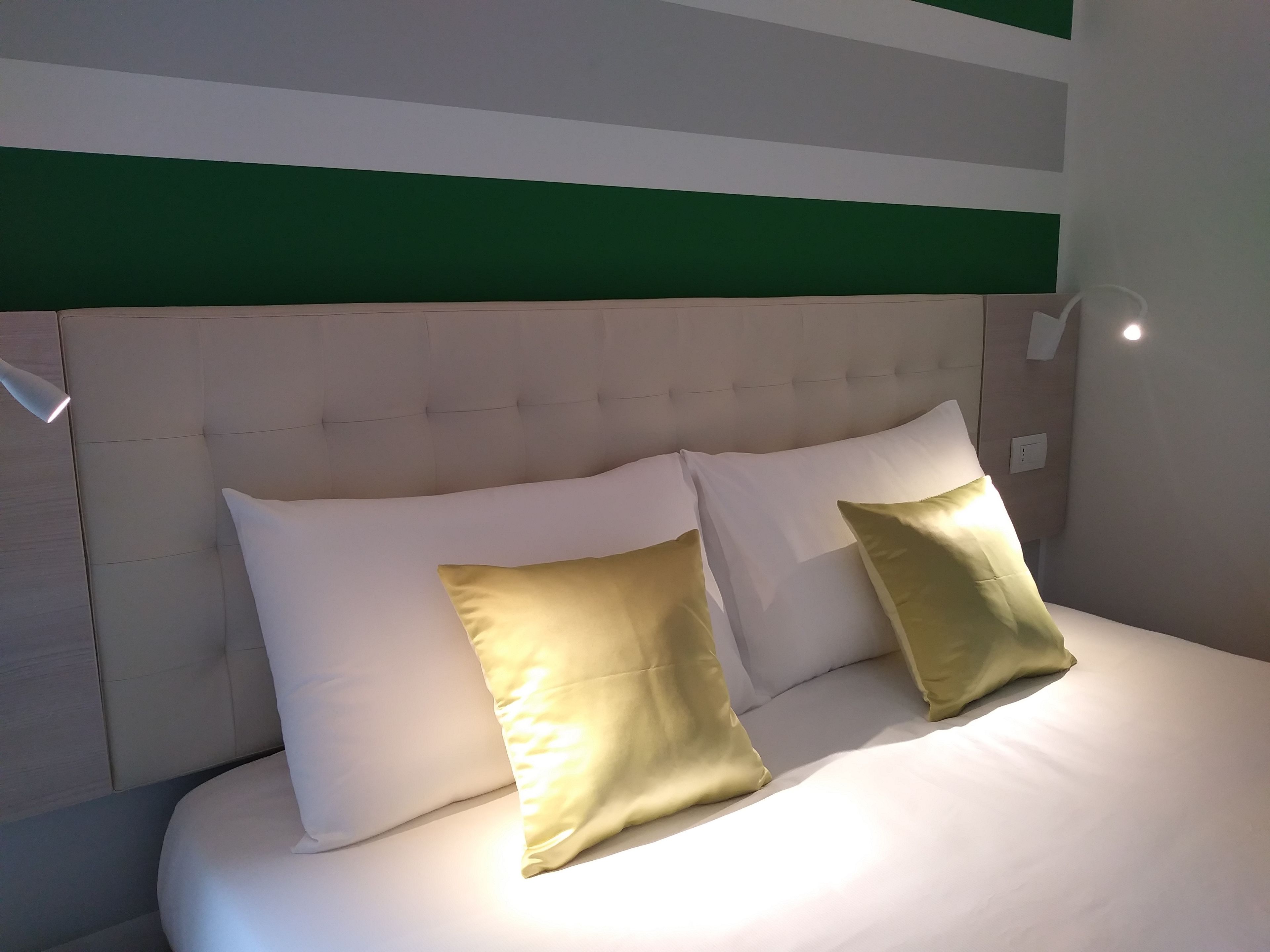 A neatly made bed with white and gold pillows, a tufted headboard, and a green accent wall.