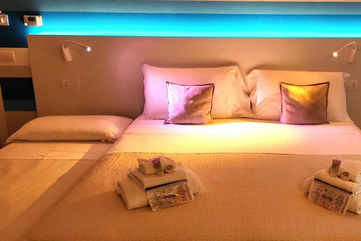 Una habitación de hotel con una cama bien hecha, dos toallas con personajes de dibujos animados y un techo iluminado en azul.
