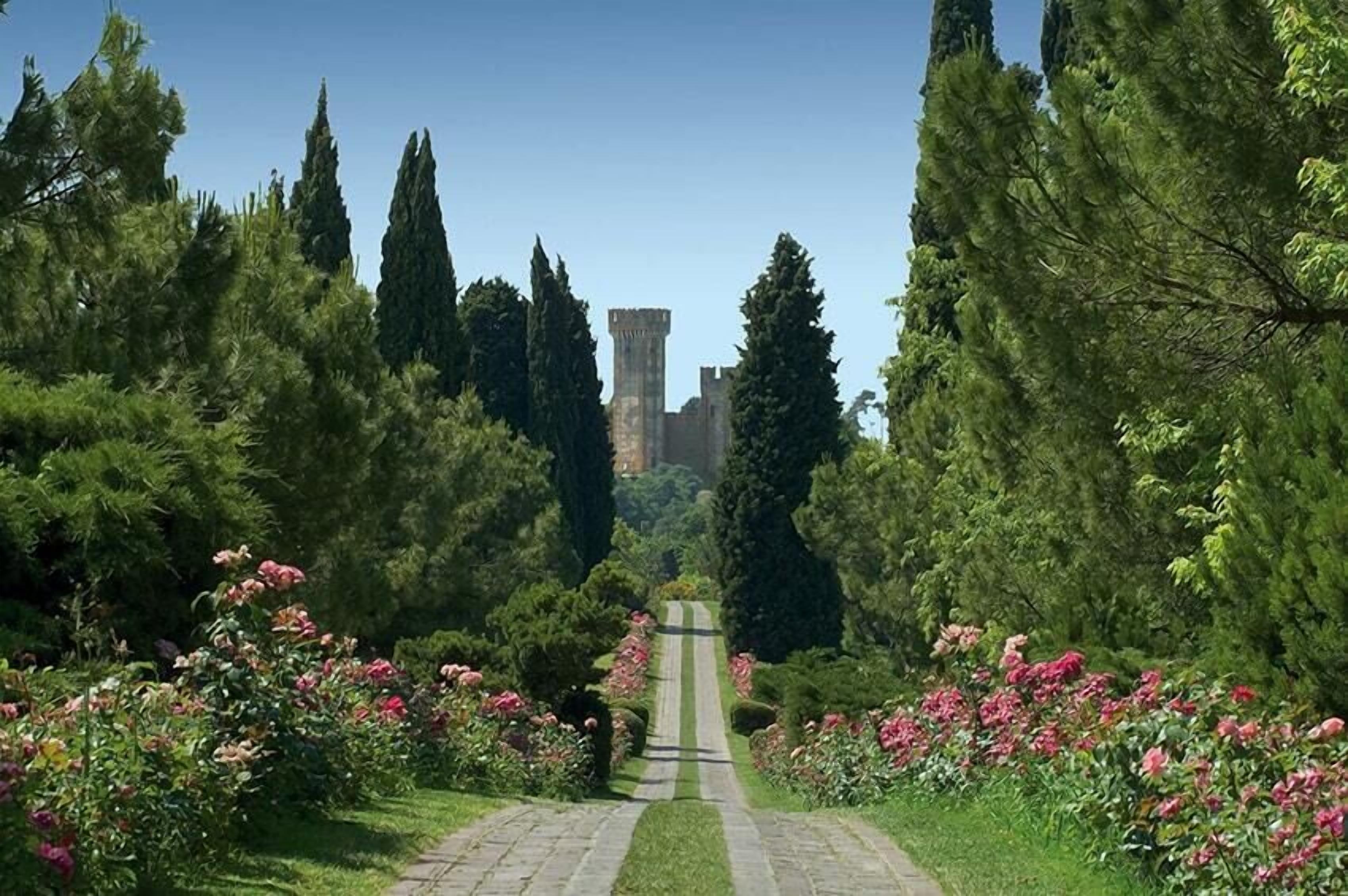 A pathway leading to a castle-like structure surrounded by lush greenery and flowering plants.