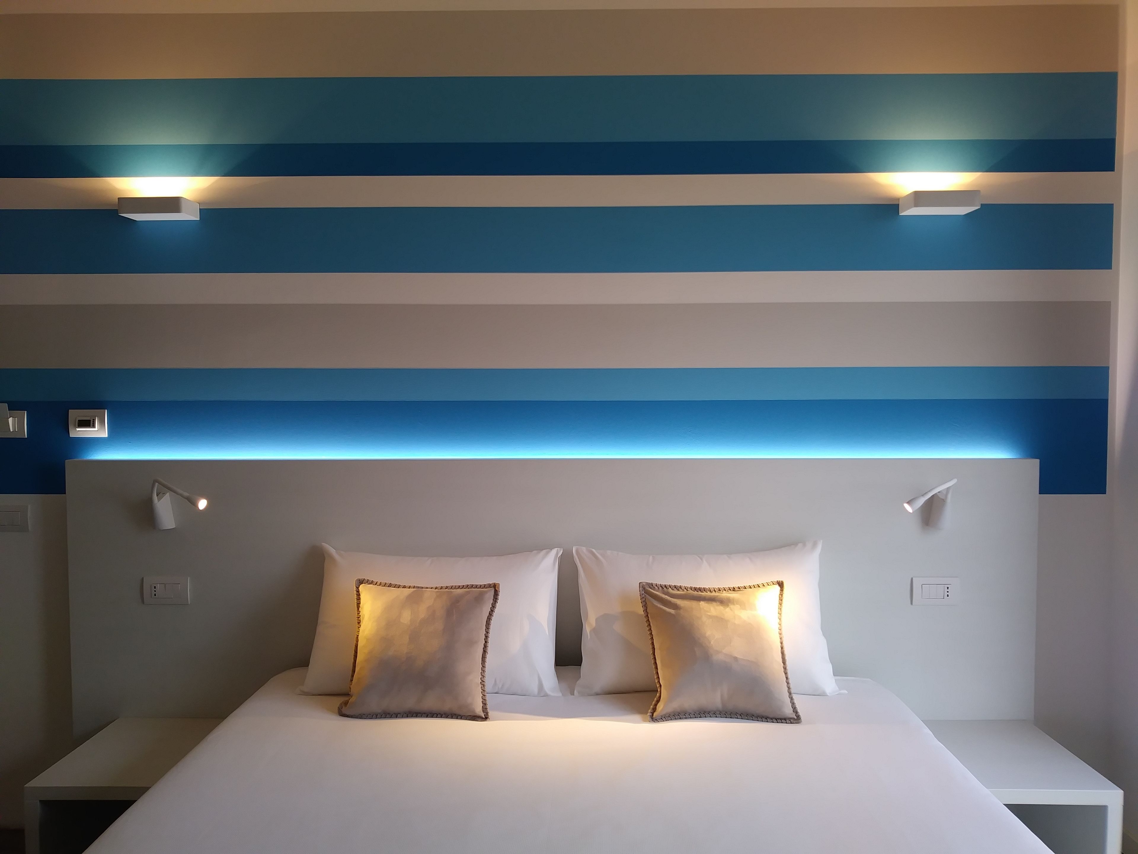 Ett hotellrum med randiga väggar, en stor säng med två kuddar och sänglampor.