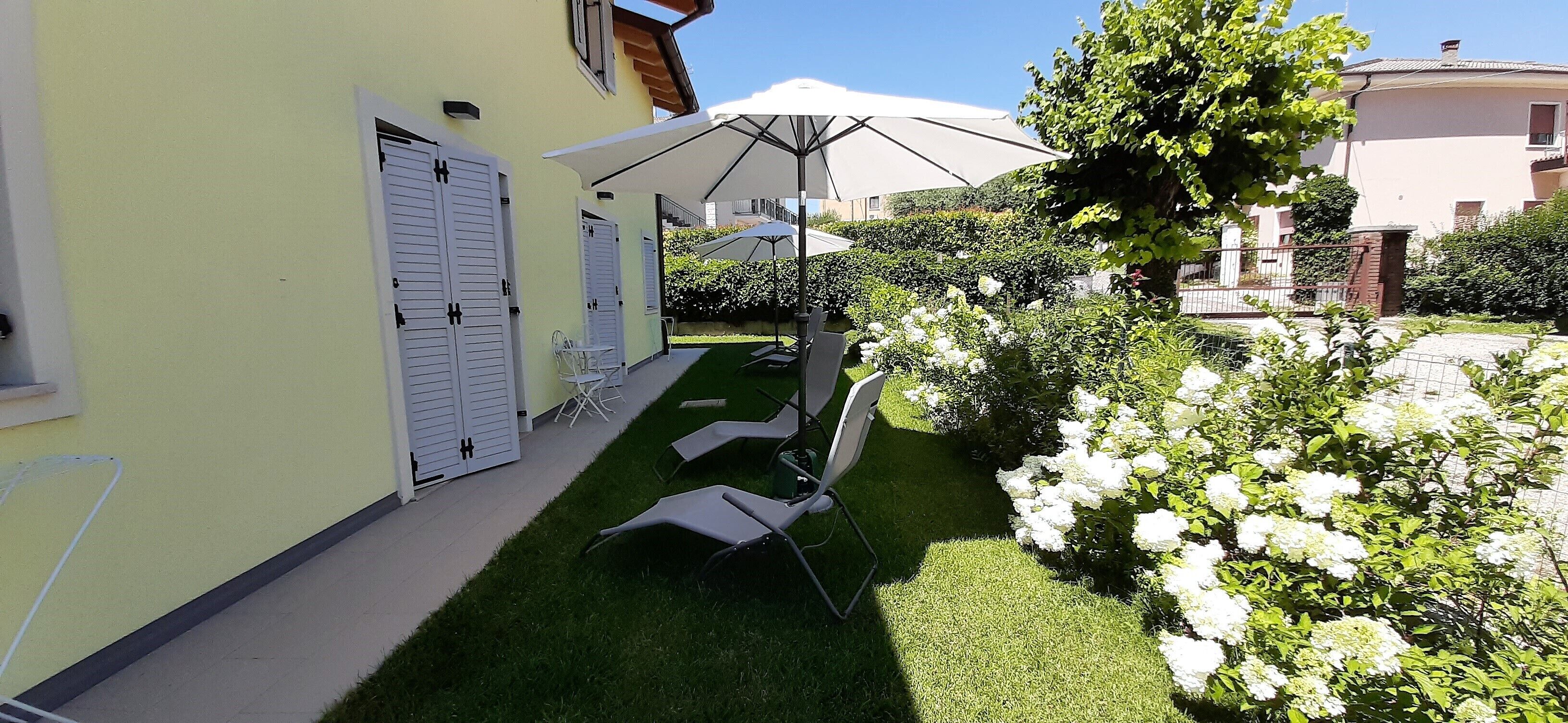 A courtyard with a lawn, white shutters, and a white umbrella.