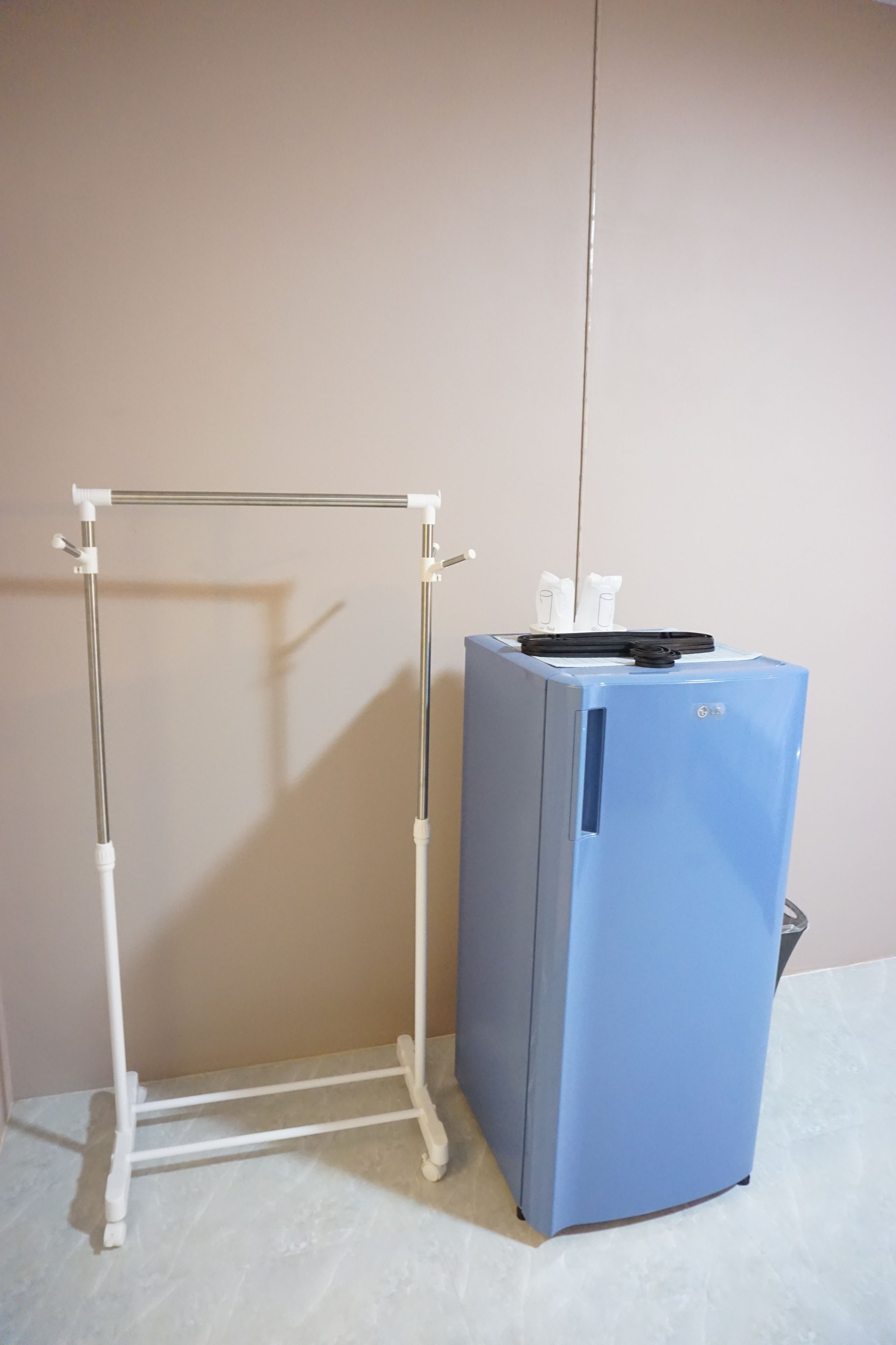 A blue refrigerator with a white metal stand against a plain wall.