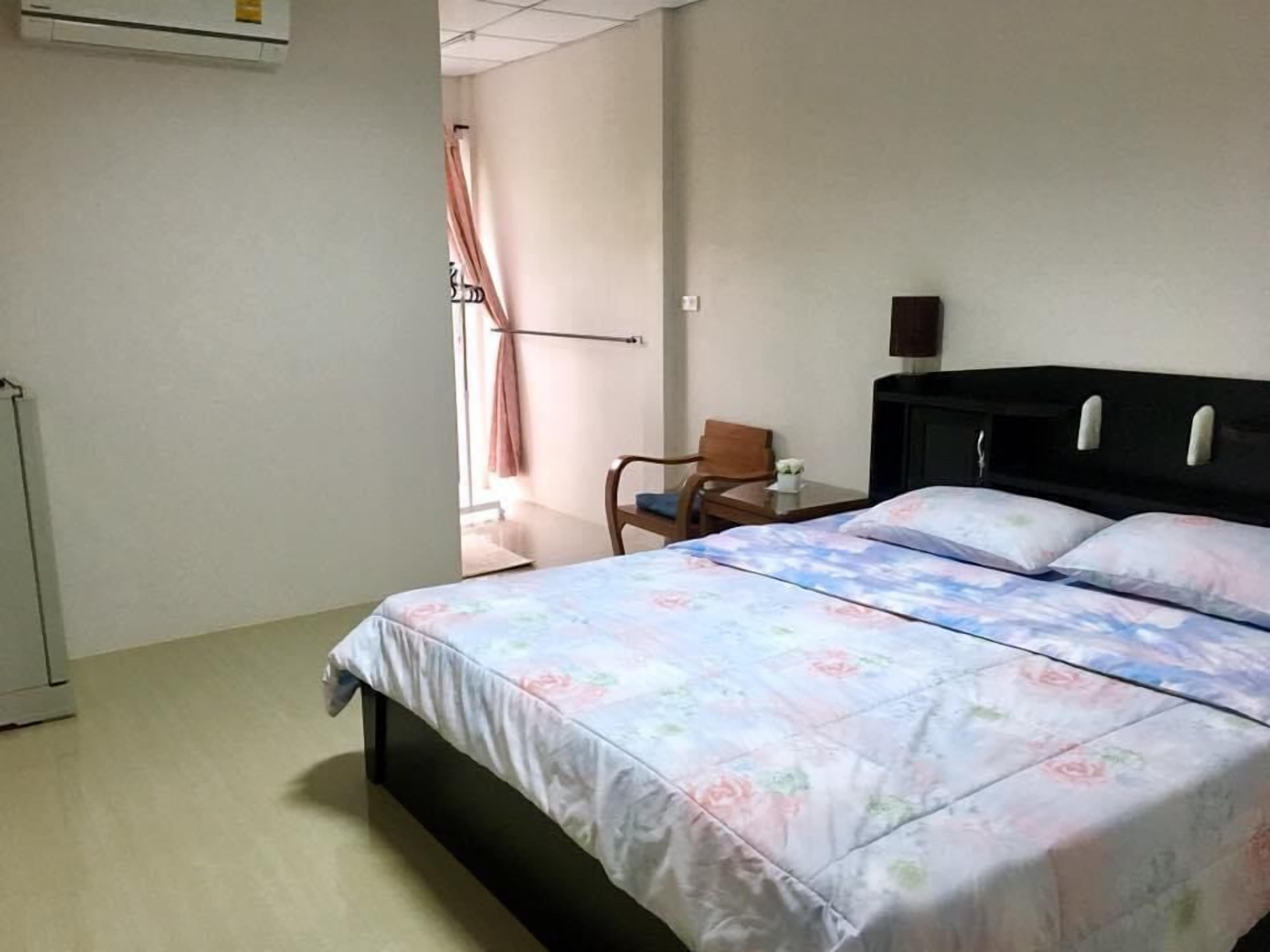 Een hotelkamer met een bed, een stoel, een nachtkastje en een wandairconditioner.