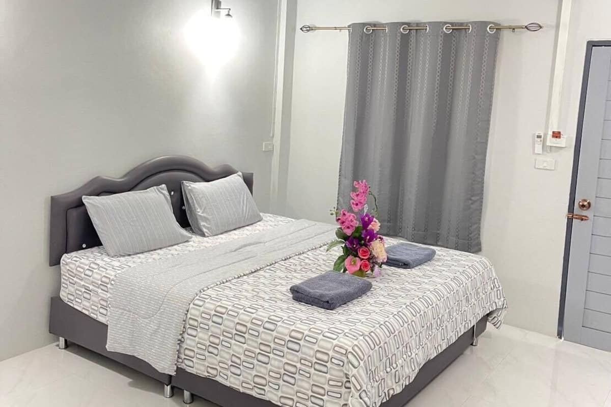 A modern bedroom with a large bed, grey curtains, and a small flower arrangement.