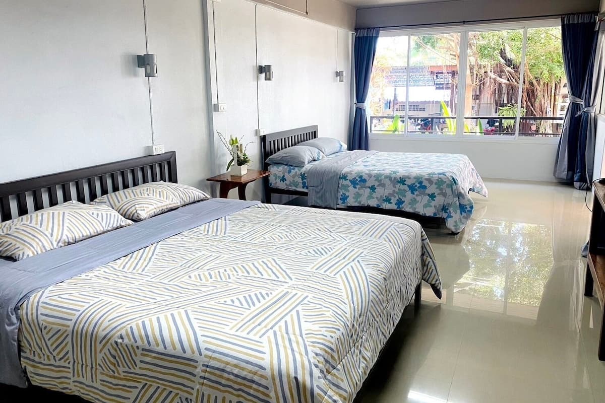 A hotel room with two beds, a small table with a plant, and a window with curtains.