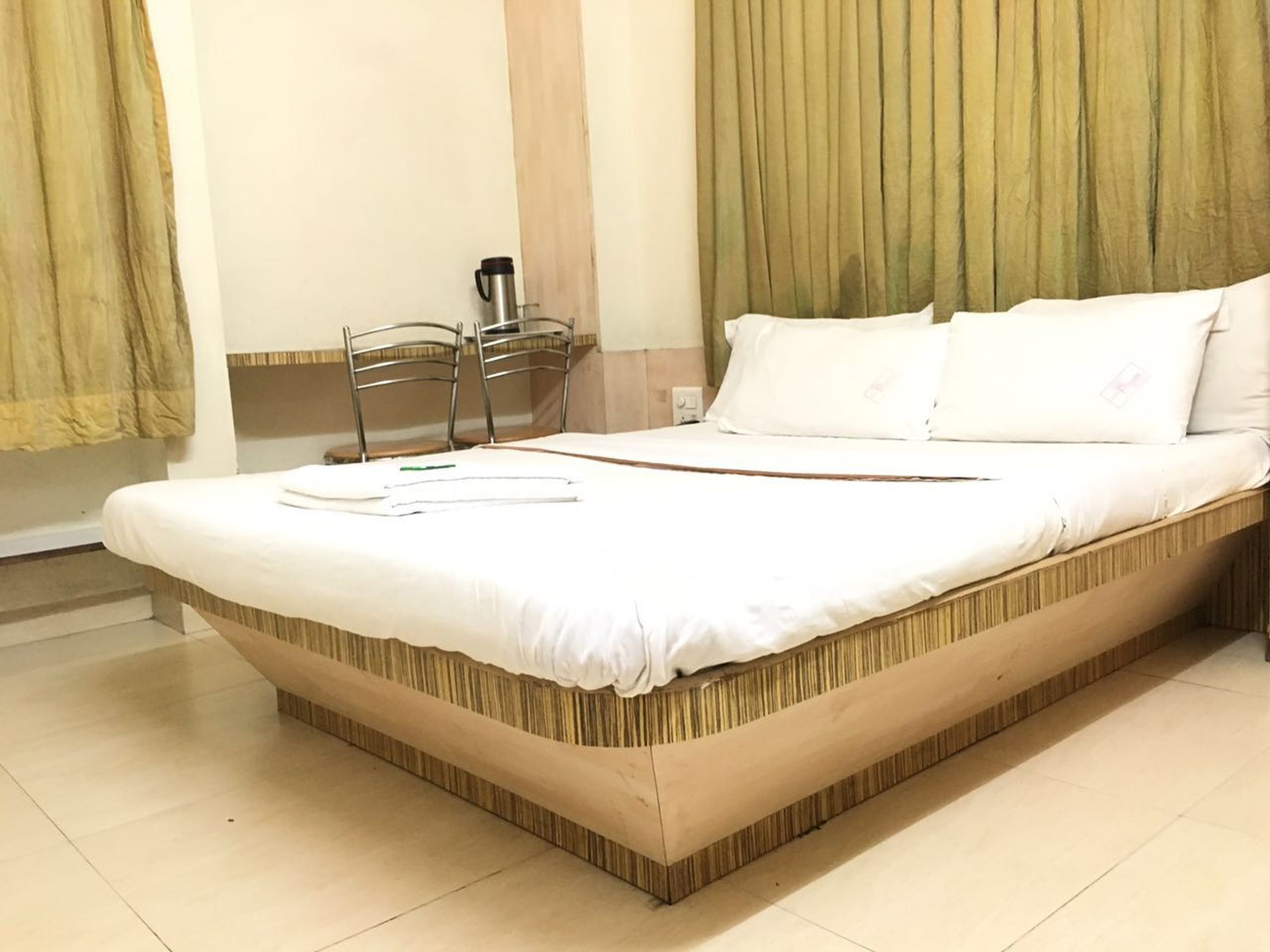 A neatly made bed with white linens, a wooden headboard, and a bedside table with a thermos.