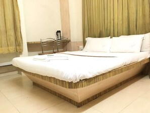 A neatly made bed with white linens, a wooden headboard, and a bedside table with a thermos. - Hotel Pranav Executive (Pune)