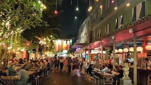 Eine belebte Straße mit Außenbereich und Essensgelegenheiten, beleuchtet von Lichterketten und Laternen.