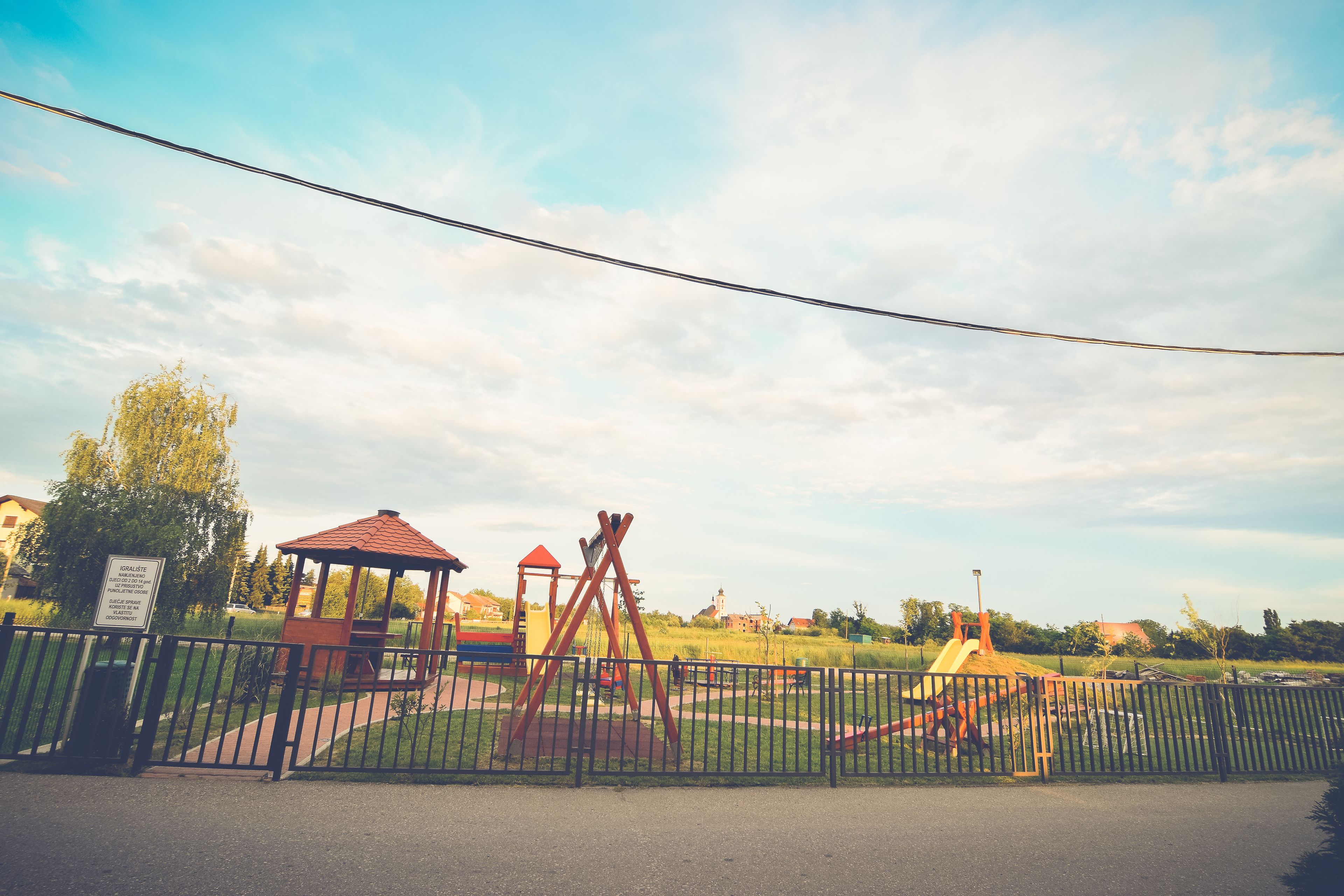 Un parque infantil vallado con columpios y un pequeño refugio.