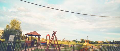 Un parque infantil vallado con columpios y un pequeño refugio.