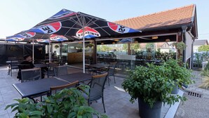 Een terras met tafels en stoelen, afgedekt door parasols, en met potplanten.