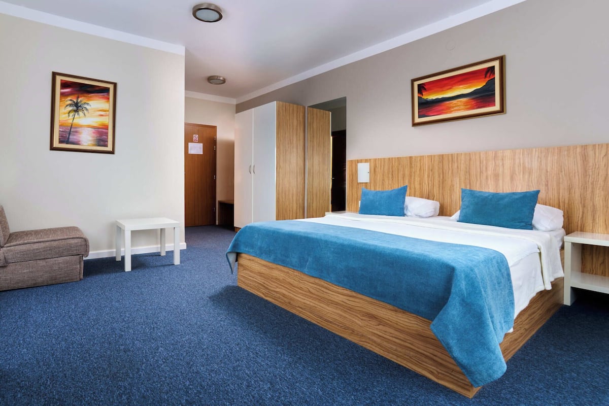 A hotel room with a large bed, a small table, a sofa, and two paintings on the walls.