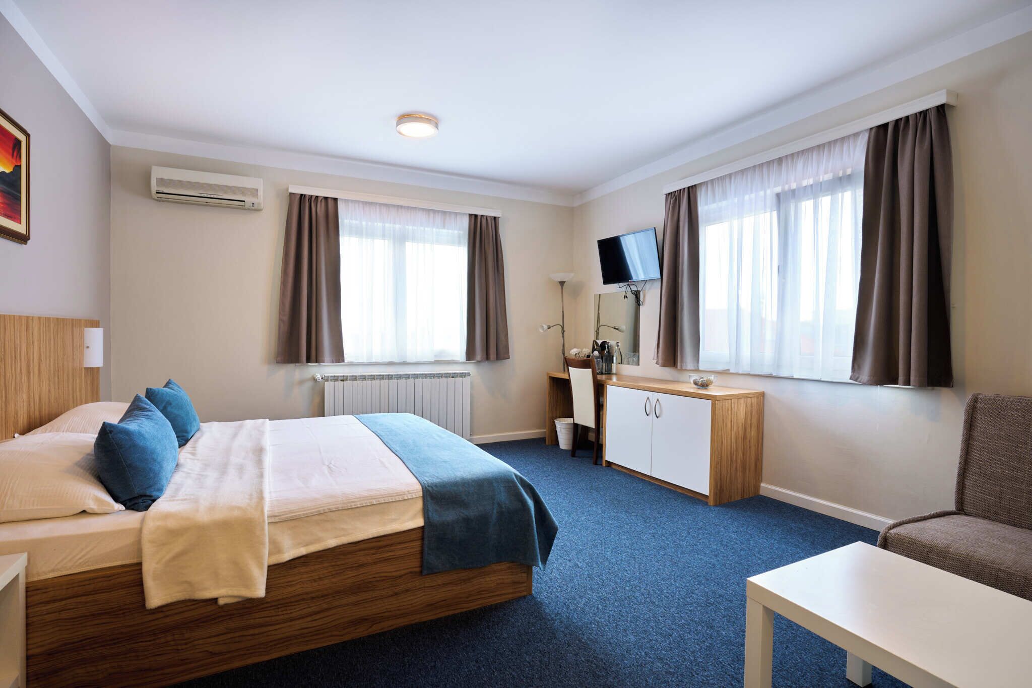 Habitación de hotel con cama, escritorio, silla, televisor y ventana con cortinas.