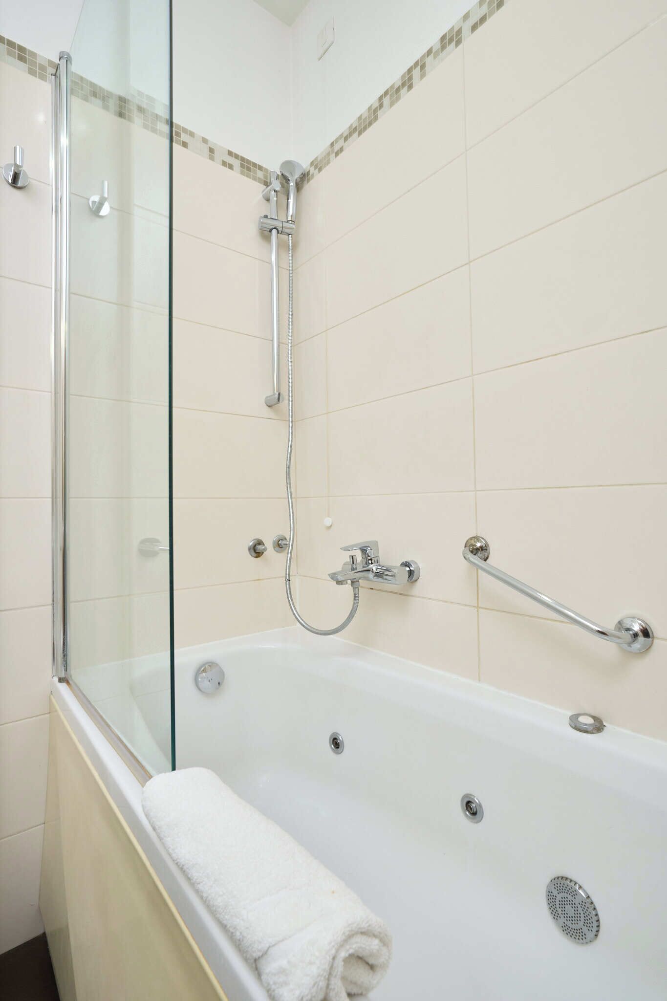 Un baño moderno con ducha de vidrio, una bañera blanca con toalla blanca e instalaciones cromadas.
