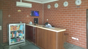 A reception area with a brick wall, a reception desk, a television, and a refrigerator stocked with beverages. - Best Budget Hotel (Abuja)