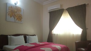 A bedroom with a bed, a chair, a painting, and an air conditioning unit. - Best Budget Hotel (Abuja)