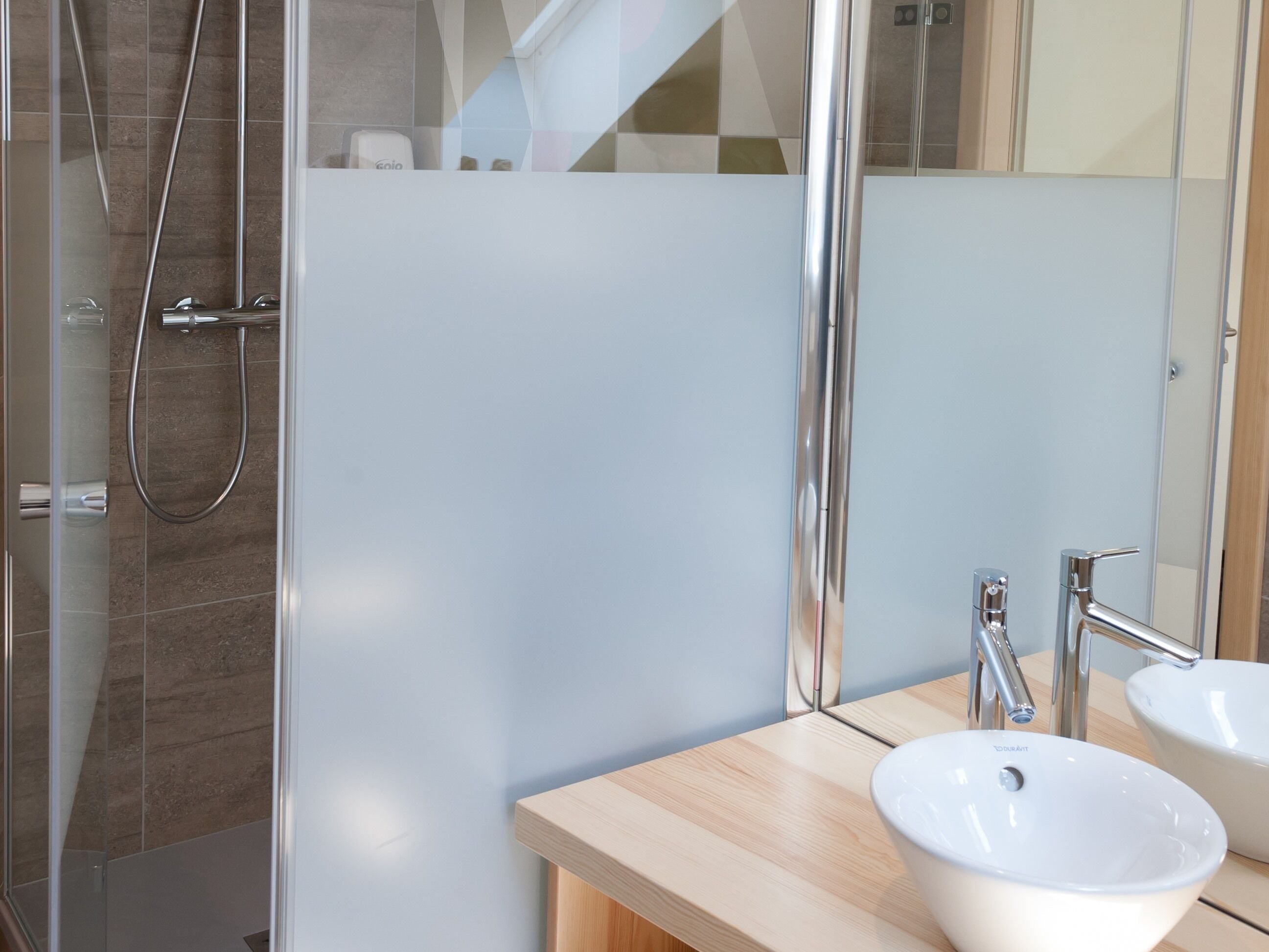 Une salle de bain moderne avec une douche à parois de verre, un meuble-lavabo en bois doté de deux vasques et un grand miroir.