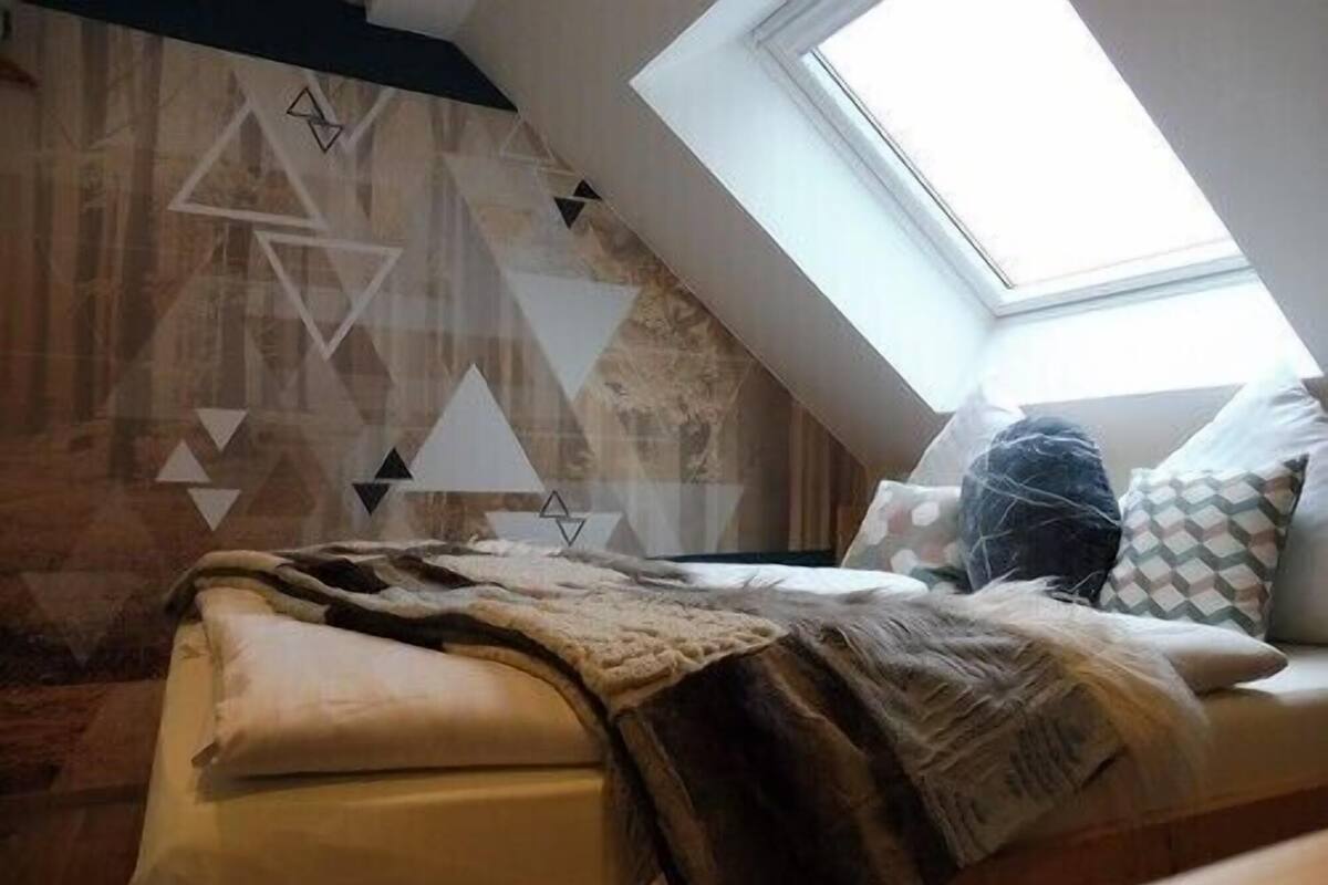 A bedroom with a sloped ceiling, a skylight, a bed with a blanket, and a geometric wall design.