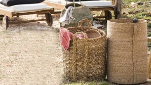 Een houten constructie aan het strand met een hangmat, ligstoelen en gevlochten manden.