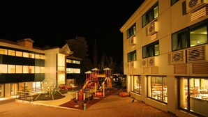 A children's playground area adjacent to a building with large windows and a brick pathway.
