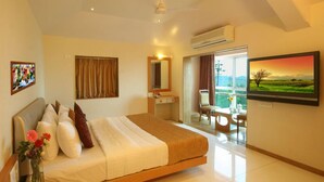 A hotel room with a bed, a desk, a chair, a window with curtains, an air conditioning unit, and a painting on the wall.