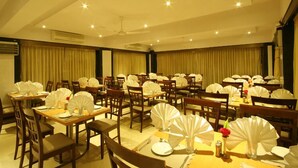 A hotel dining area with multiple tables set for service, each with white tablecloths, chairs, and decorative fans.