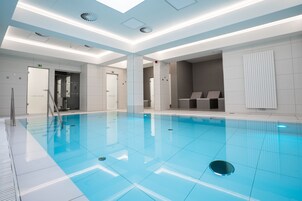 Una piscina interior moderna con agua azul cristalina, paredes con azulejos e iluminación empotrada en el techo.