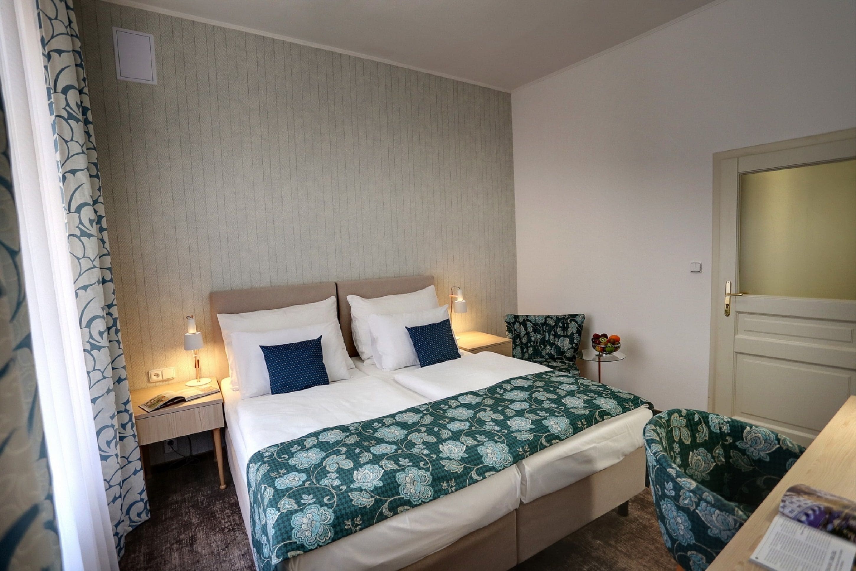 Una habitación de hotel con cama, mesita de noche, una silla y una pequeña mesa con un frutero.