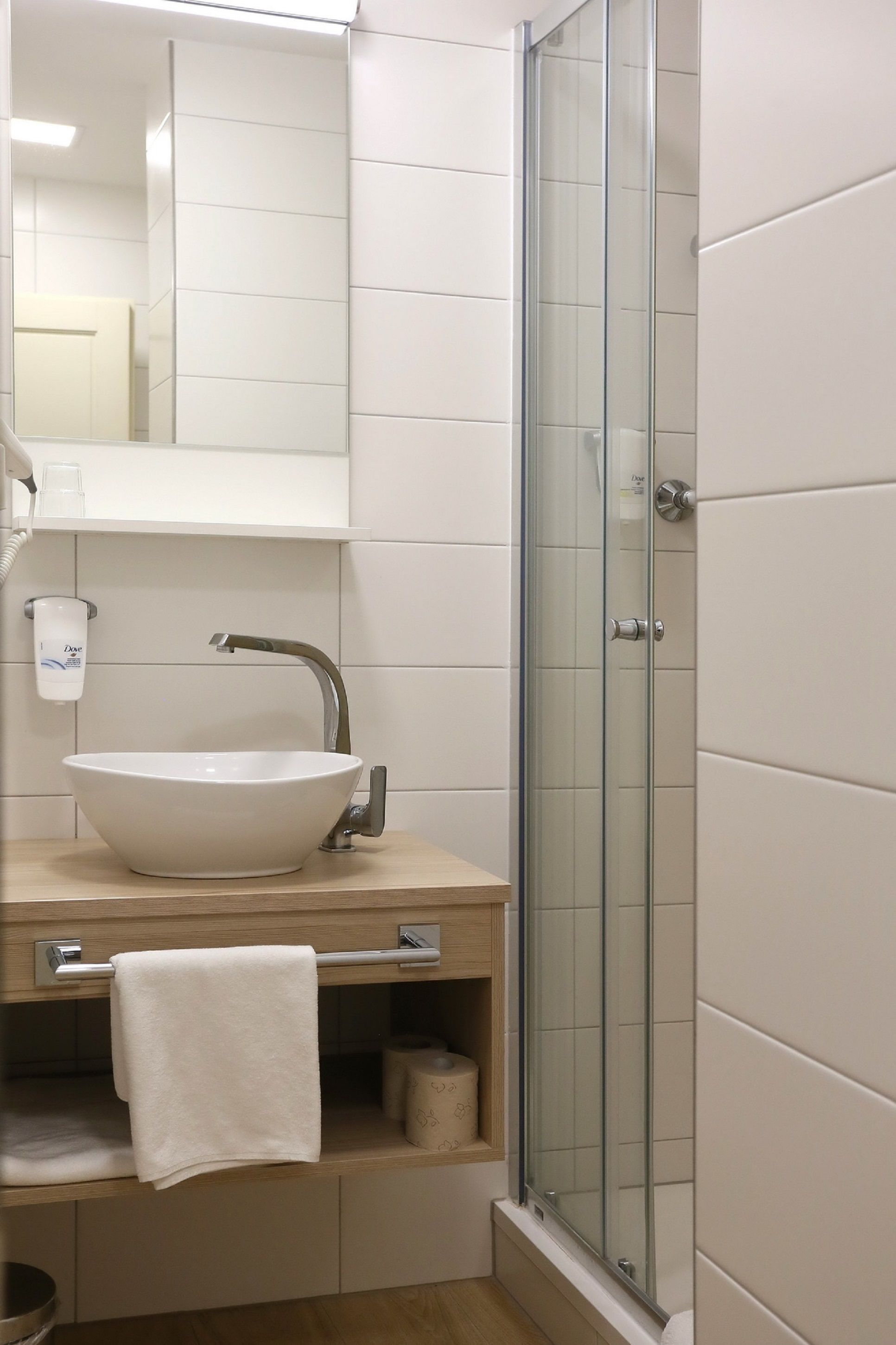 Ein Badezimmer mit einem weißen Waschbecken, einer Duschkabine aus Glas und einem Spiegel über dem Waschbecken.