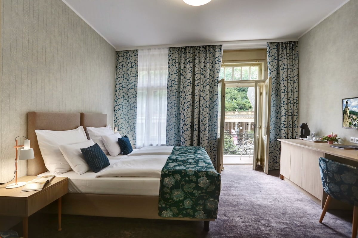 A hotel room with a bed, bedside table, lamp, and a desk with a chair.