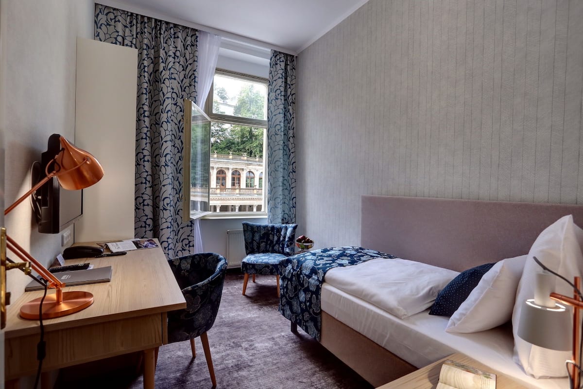 A hotel room with a bed, desk, chair, and a window with curtains.
