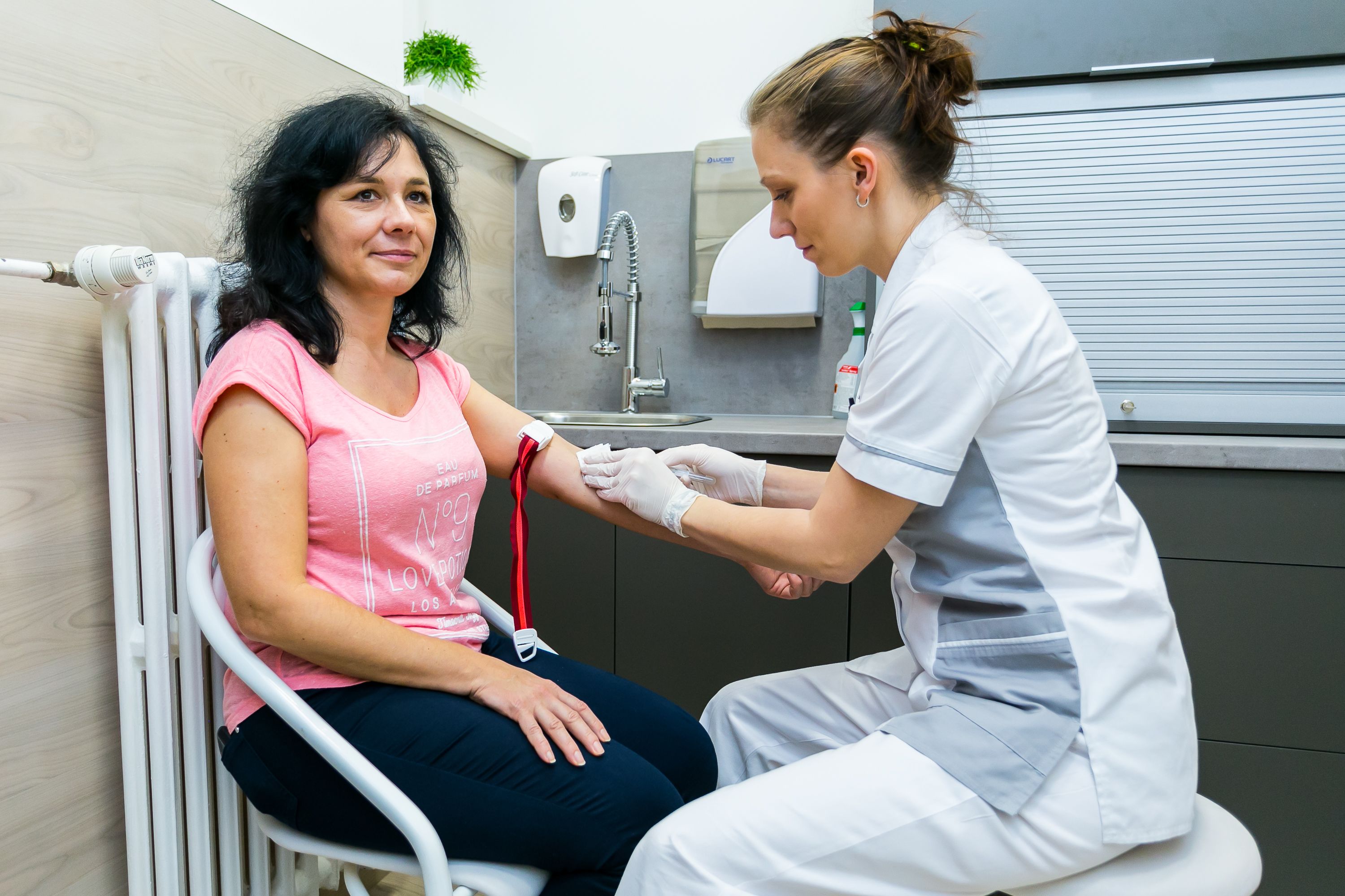 A person receiving a medical procedure in a clinical setting with a sink and medical supplies in the background.