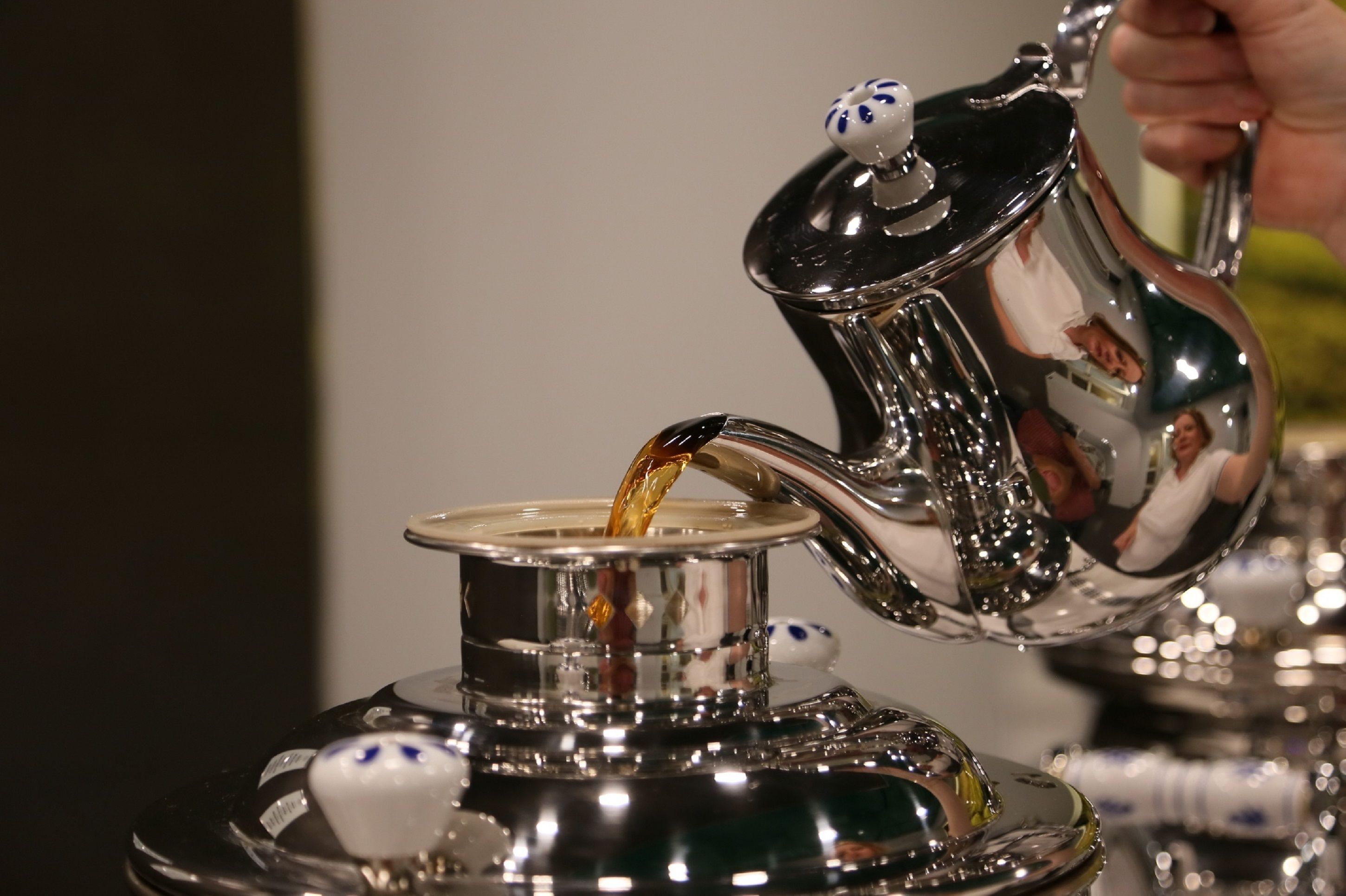 A silver teapot pouring tea into a matching cup.