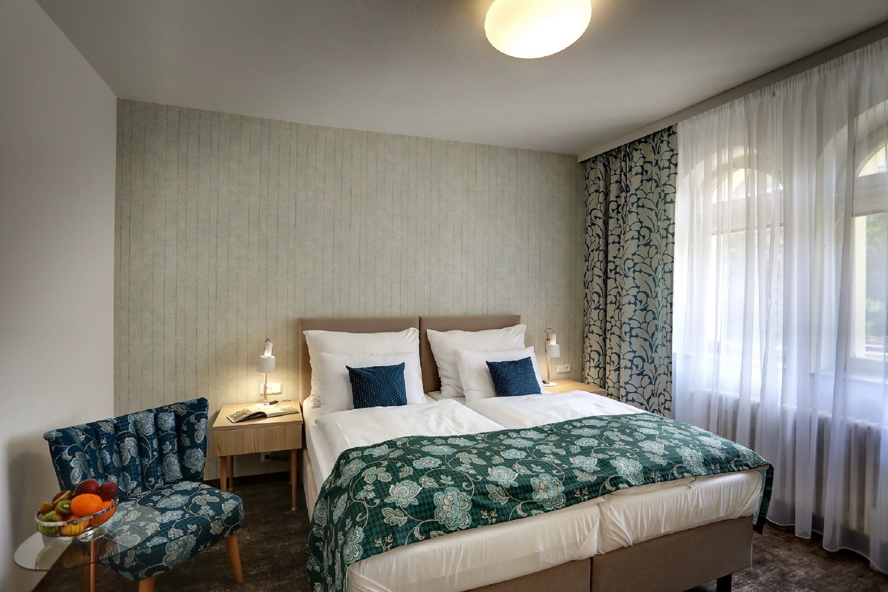 A hotel room with a bed, bedside tables, a chair, and a window with curtains.
